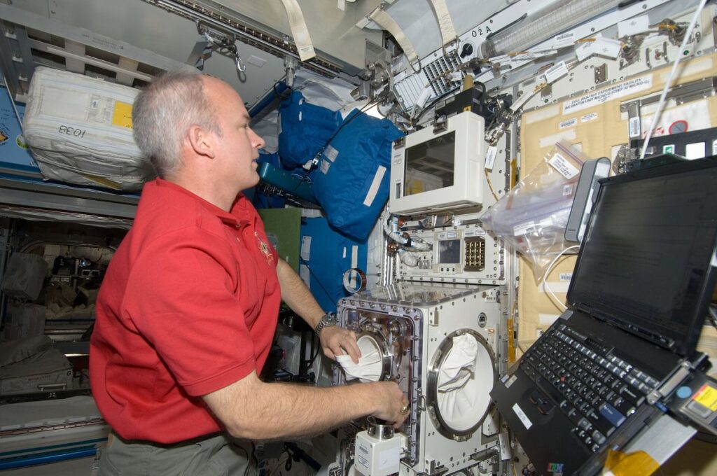 Astronauta flotando junto a un módulo de experimentos lleno de cables y equipos