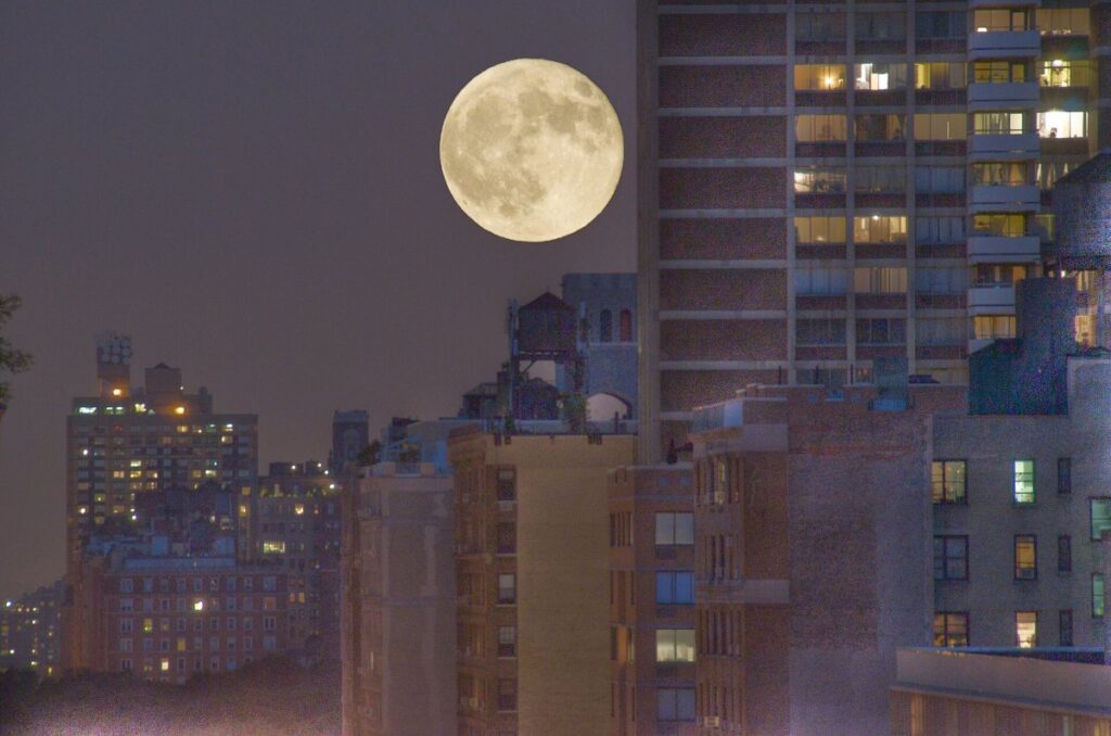 Luna llena saliendo por el horizonte detrás de una ciudad